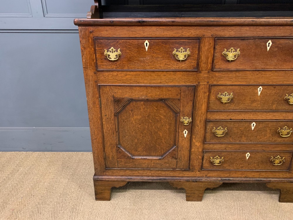 An early nineteenth-century Welsh oak dresser featuring a three-tier open plate rack above a base with drawers, cupboards, and brass hardware. View V
