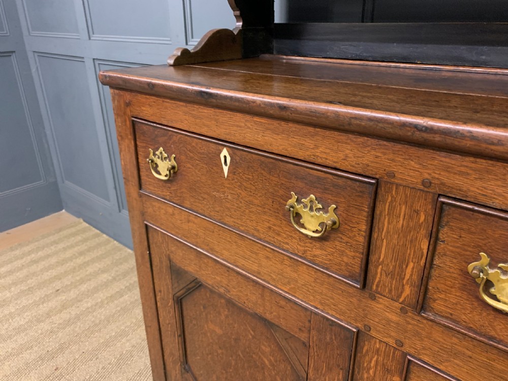 An early nineteenth-century Welsh oak dresser featuring a three-tier open plate rack above a base with drawers, cupboards, and brass hardware. View VI