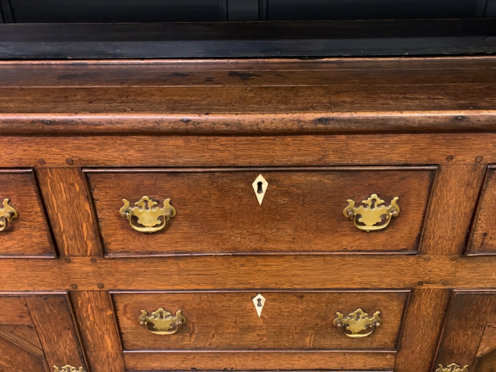 An early nineteenth-century Welsh oak dresser featuring a three-tier open plate rack above a base with drawers, cupboards, and brass hardware. View VII