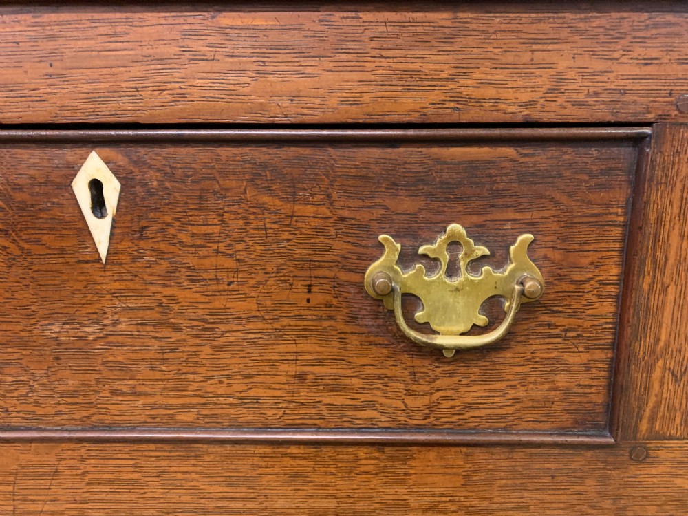 An early nineteenth-century Welsh oak dresser featuring a three-tier open plate rack above a base with drawers, cupboards, and brass hardware. View X