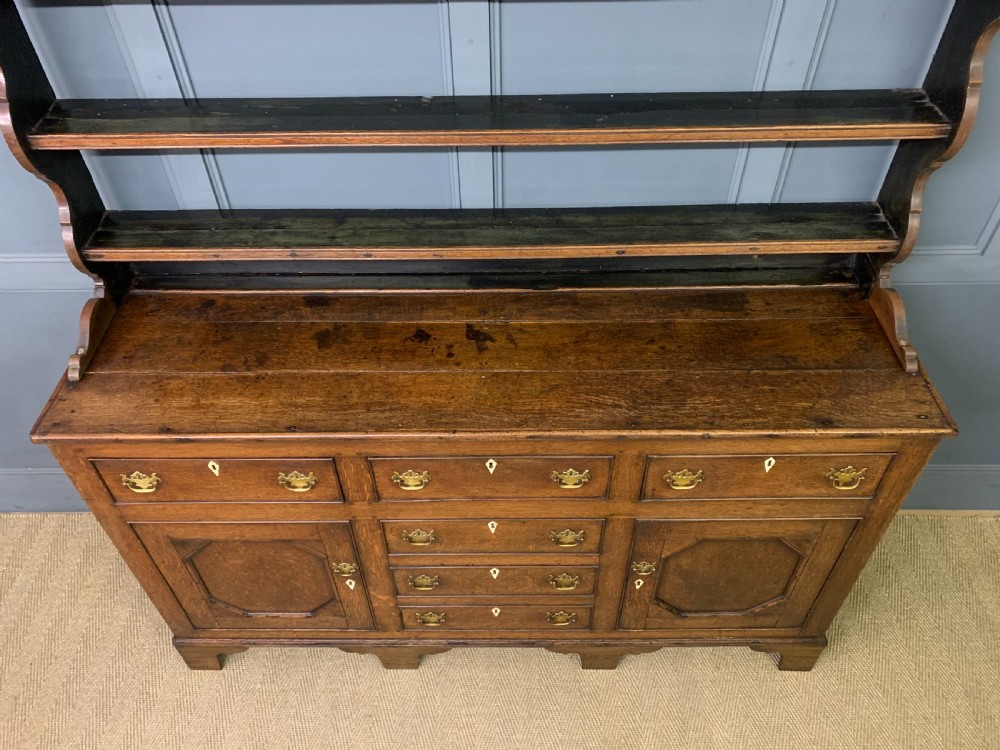 An early nineteenth-century Welsh oak dresser featuring a three-tier open plate rack above a base with drawers, cupboards, and brass hardware. View XI