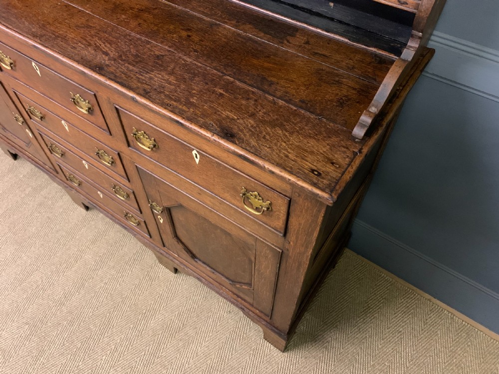 An early nineteenth-century Welsh oak dresser featuring a three-tier open plate rack above a base with drawers, cupboards, and brass hardware. View XII