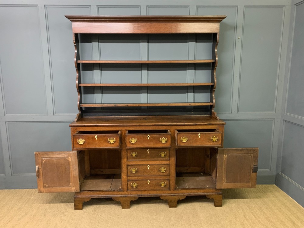 An early nineteenth-century Welsh oak dresser featuring a three-tier open plate rack above a base with drawers, cupboards, and brass hardware. View XIV