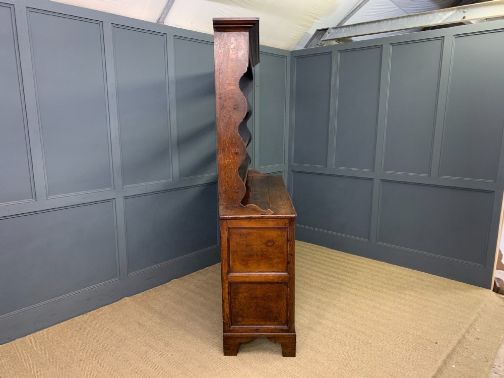An early nineteenth-century Welsh oak dresser featuring a three-tier open plate rack above a base with drawers, cupboards, and brass hardware. View XVI