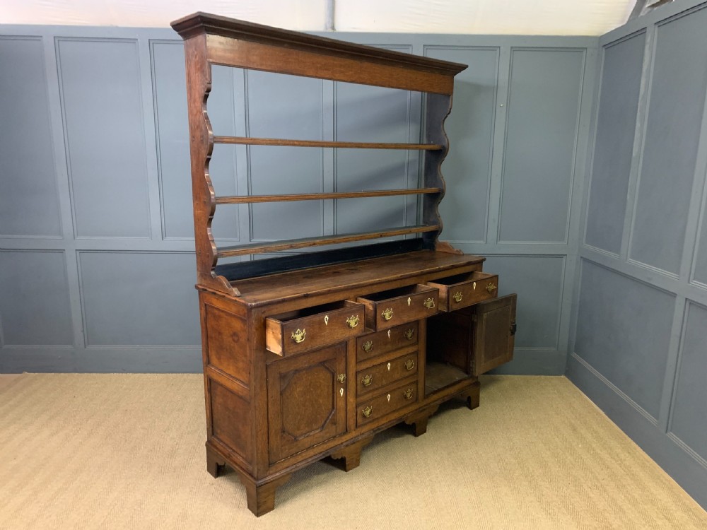An early nineteenth-century Welsh oak dresser featuring a three-tier open plate rack above a base with drawers, cupboards, and brass hardware. View XVIII