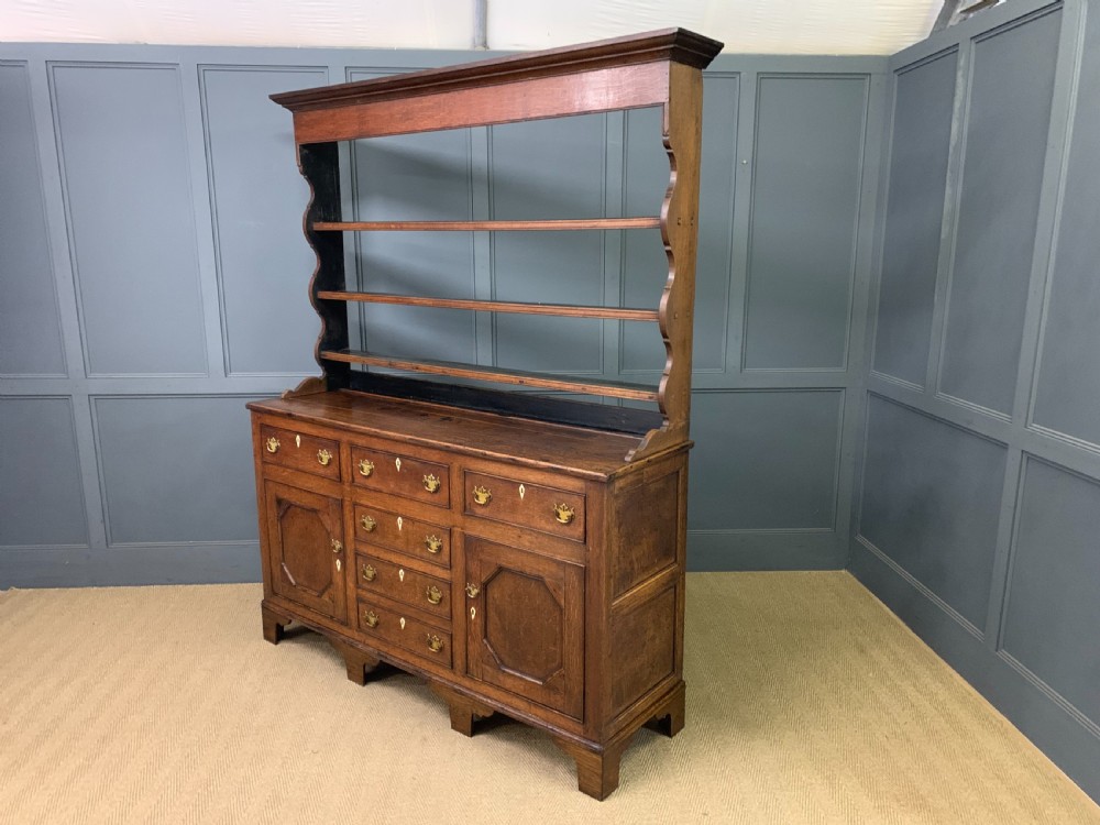 An early nineteenth-century Welsh oak dresser featuring a three-tier open plate rack above a base with drawers, cupboards, and brass hardware. View XIX