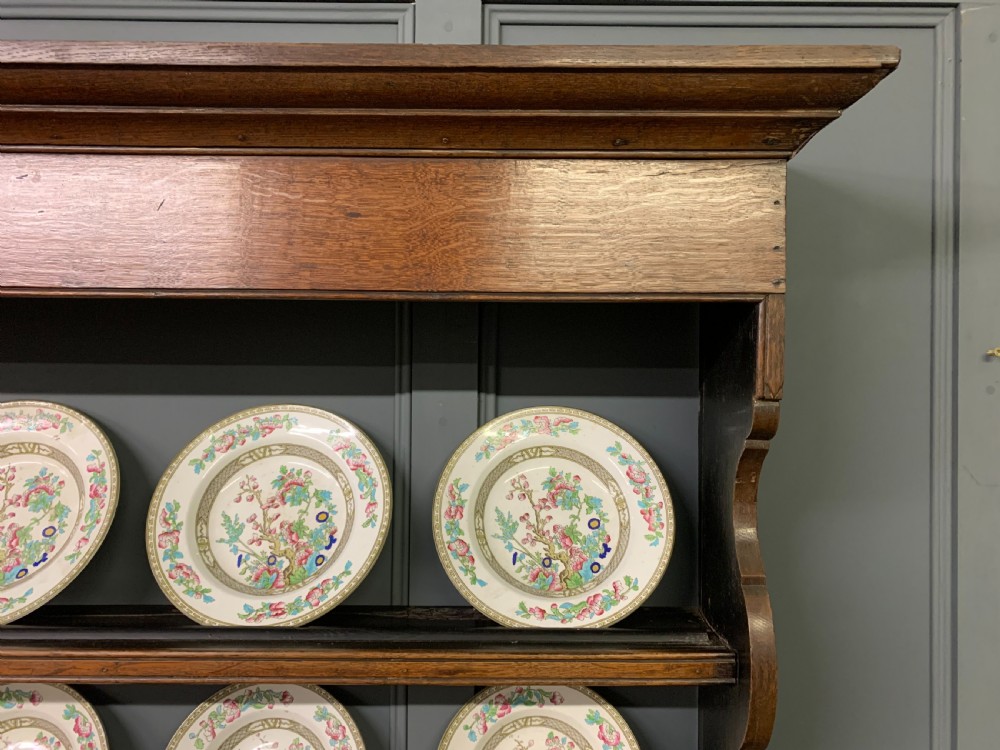 An early nineteenth-century Welsh oak dresser featuring a three-tier open plate rack above a base with drawers, cupboards, and brass hardware. View XXI