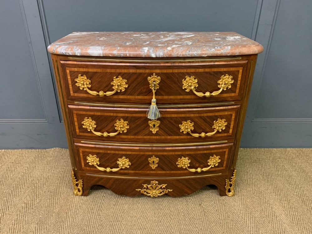 A French Louis XV style kingwood commode featuring three drawers, gilded metal mounts, and a variegated pink marble top.