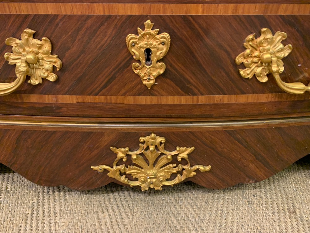 A French Louis XV style kingwood commode featuring three drawers, gilded metal mounts, and a variegated pink marble top. View IV