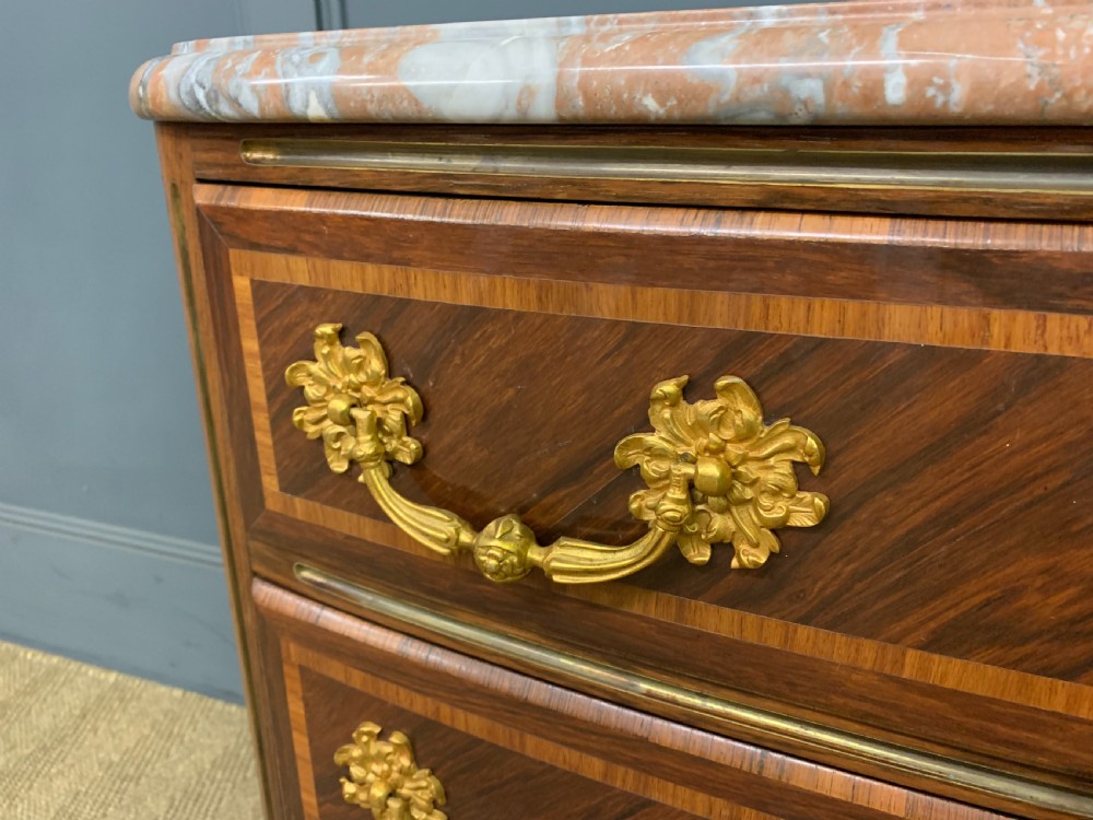 A French Louis XV style kingwood commode featuring three drawers, gilded metal mounts, and a variegated pink marble top. View V