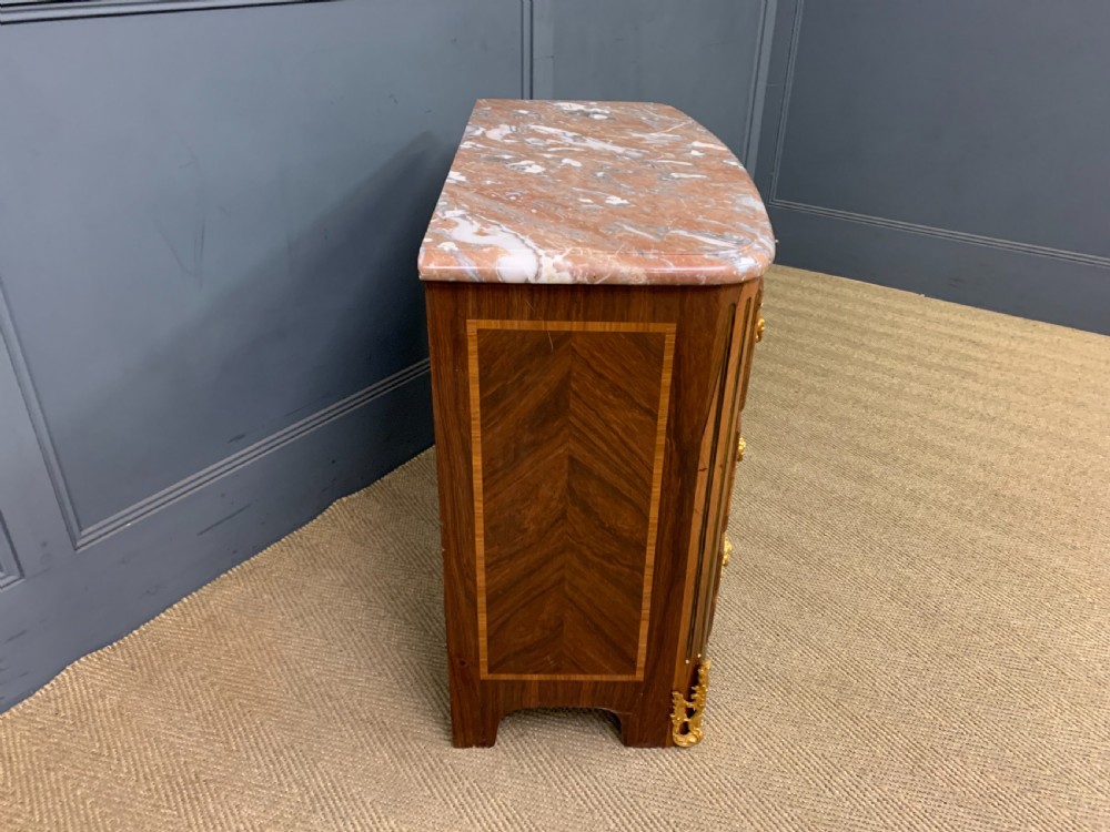 A French Louis XV style kingwood commode featuring three drawers, gilded metal mounts, and a variegated pink marble top. View VII