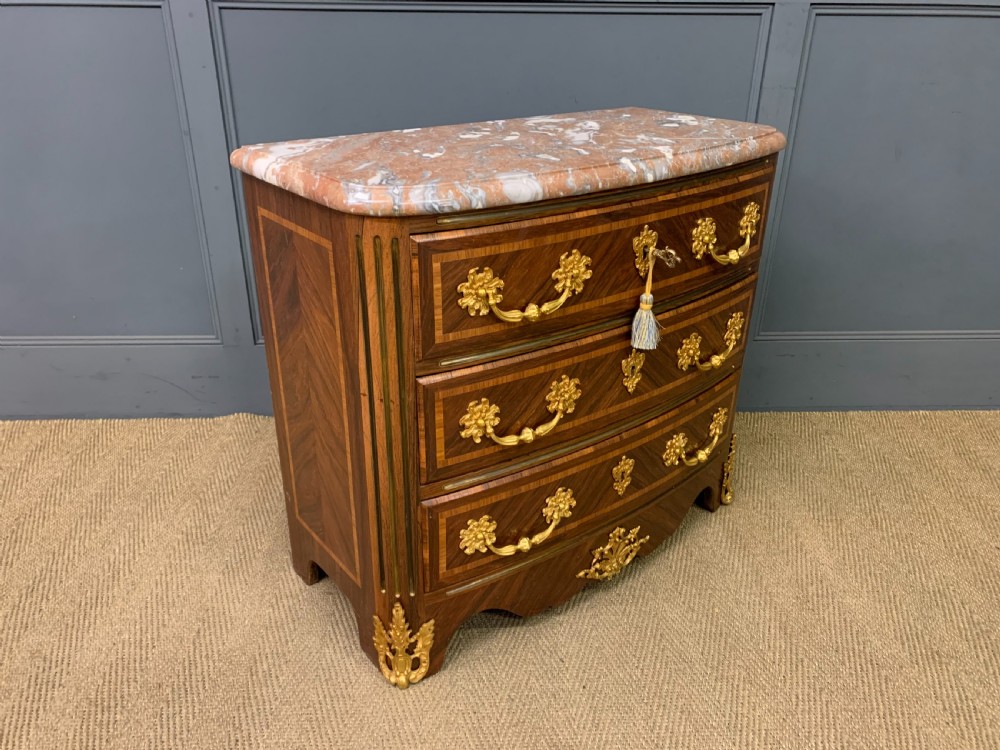 A French Louis XV style kingwood commode featuring three drawers, gilded metal mounts, and a variegated pink marble top. View VIII
