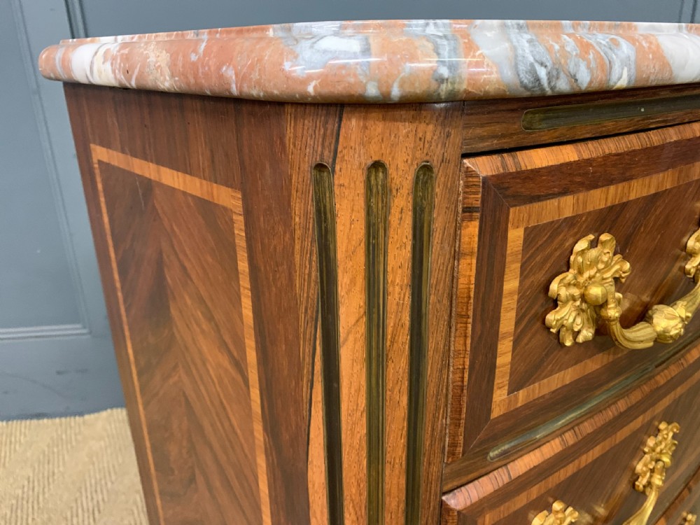 A French Louis XV style kingwood commode featuring three drawers, gilded metal mounts, and a variegated pink marble top. View X