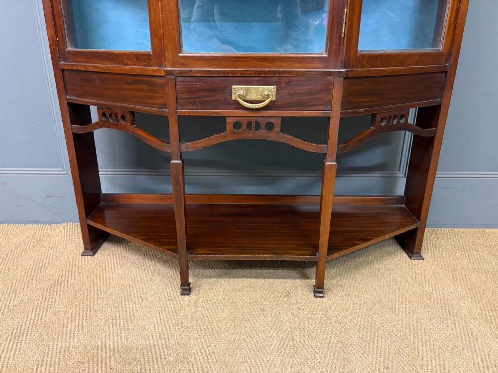 An Arts and Crafts mahogany display cabinet with stylized blue and green stained glass top panels, three glazed doors, and a blue fabric-lined interior. View III