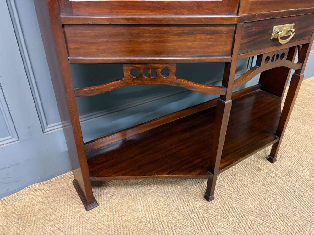 An Arts and Crafts mahogany display cabinet with stylized blue and green stained glass top panels, three glazed doors, and a blue fabric-lined interior. View V