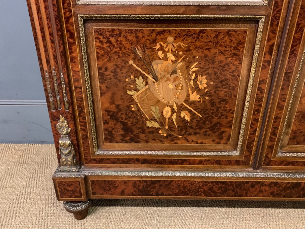A 19th-century French double-door bookcase featuring amboyna and mahogany veneers, intricate floral marquetry, pleated cream fabric door panels, and brass mounts. View IV