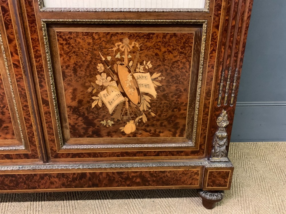 A 19th-century French double-door bookcase featuring amboyna and mahogany veneers, intricate floral marquetry, pleated cream fabric door panels, and brass mounts. View V