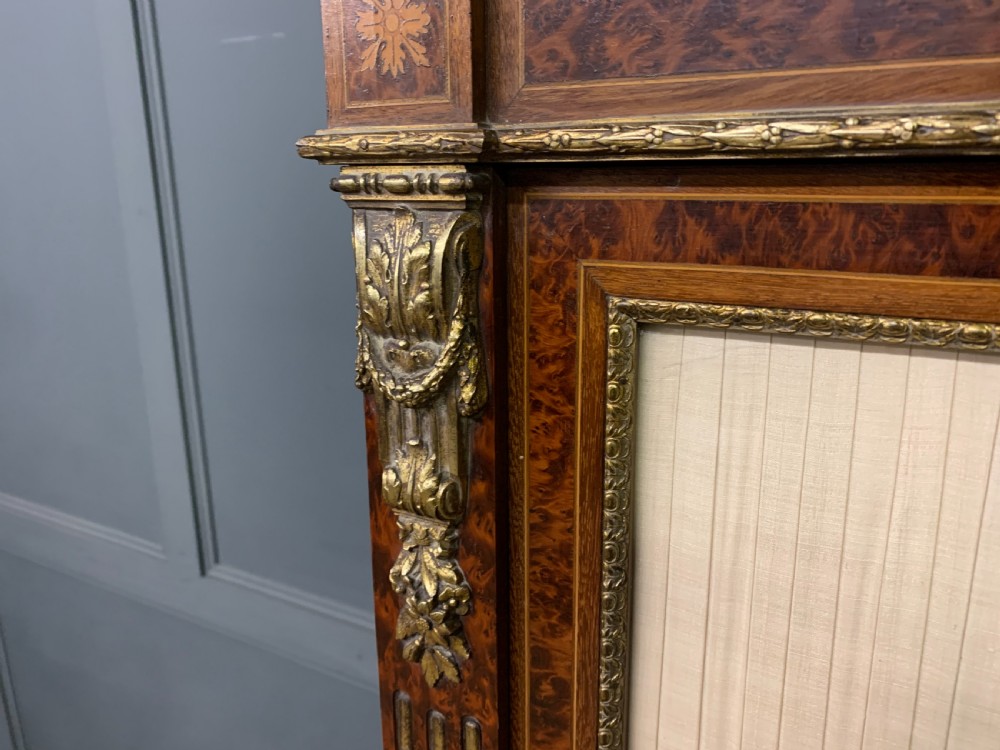 A 19th-century French double-door bookcase featuring amboyna and mahogany veneers, intricate floral marquetry, pleated cream fabric door panels, and brass mounts. View X