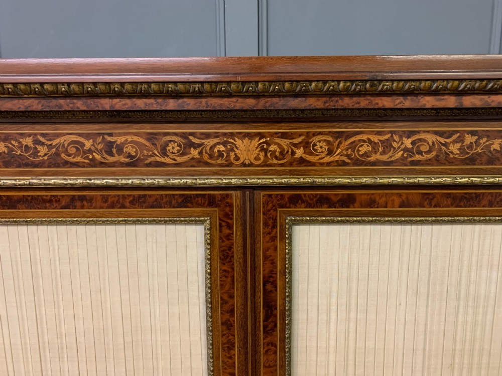 A 19th-century French double-door bookcase featuring amboyna and mahogany veneers, intricate floral marquetry, pleated cream fabric door panels, and brass mounts. View XI