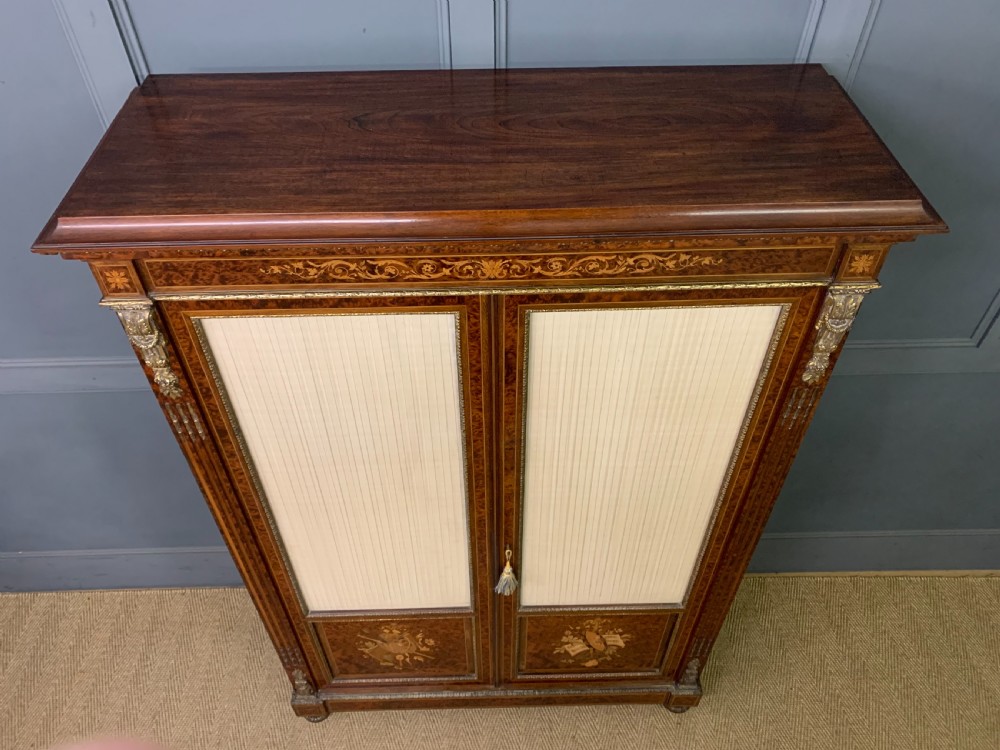 A 19th-century French double-door bookcase featuring amboyna and mahogany veneers, intricate floral marquetry, pleated cream fabric door panels, and brass mounts. View XIII