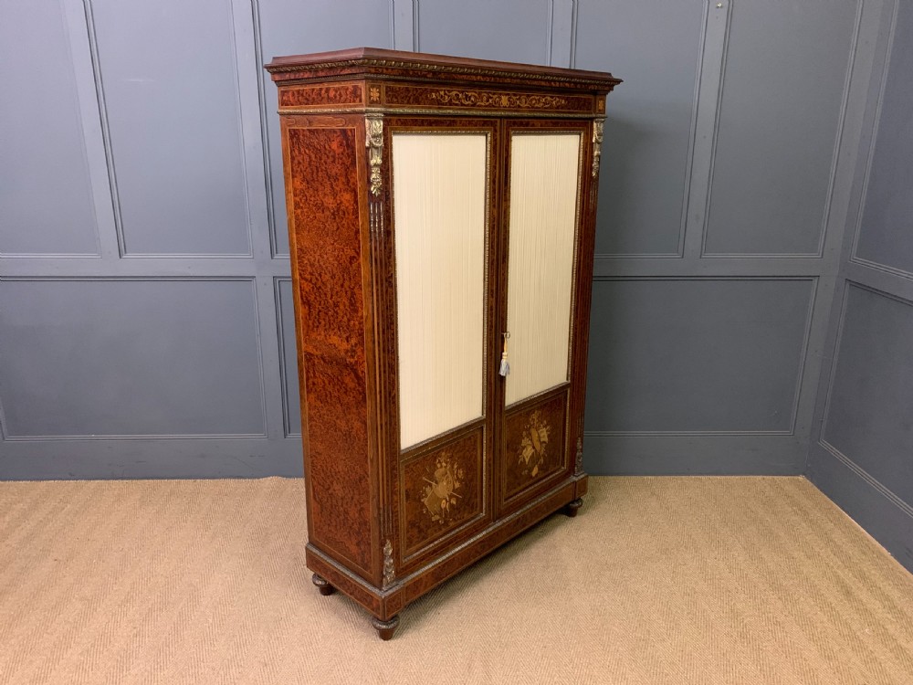 A 19th-century French double-door bookcase featuring amboyna and mahogany veneers, intricate floral marquetry, pleated cream fabric door panels, and brass mounts. View XIV
