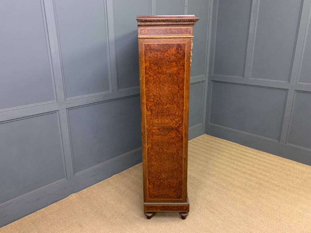 A 19th-century French double-door bookcase featuring amboyna and mahogany veneers, intricate floral marquetry, pleated cream fabric door panels, and brass mounts. View XV