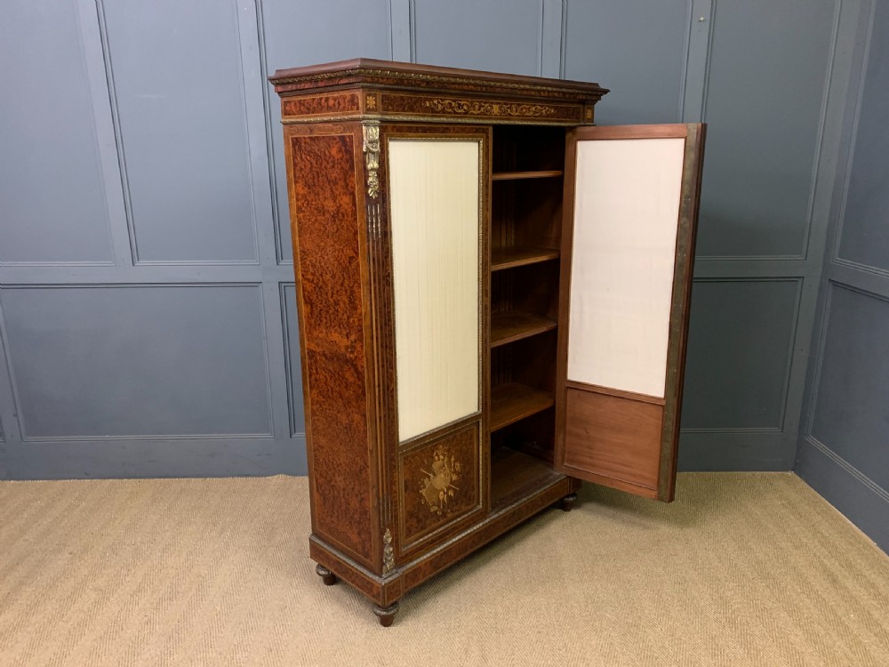 A 19th-century French double-door bookcase featuring amboyna and mahogany veneers, intricate floral marquetry, pleated cream fabric door panels, and brass mounts. View XVII