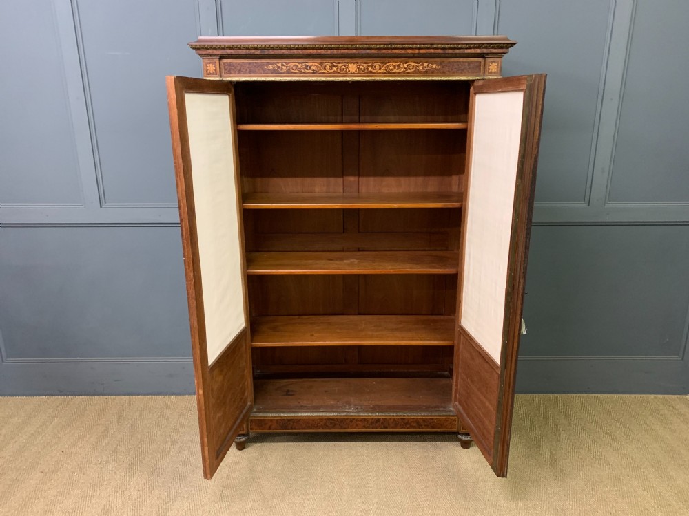 A 19th-century French double-door bookcase featuring amboyna and mahogany veneers, intricate floral marquetry, pleated cream fabric door panels, and brass mounts. View XX