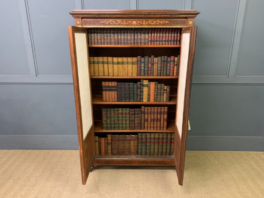 A 19th-century French double-door bookcase featuring amboyna and mahogany veneers, intricate floral marquetry, pleated cream fabric door panels, and brass mounts. View XXI