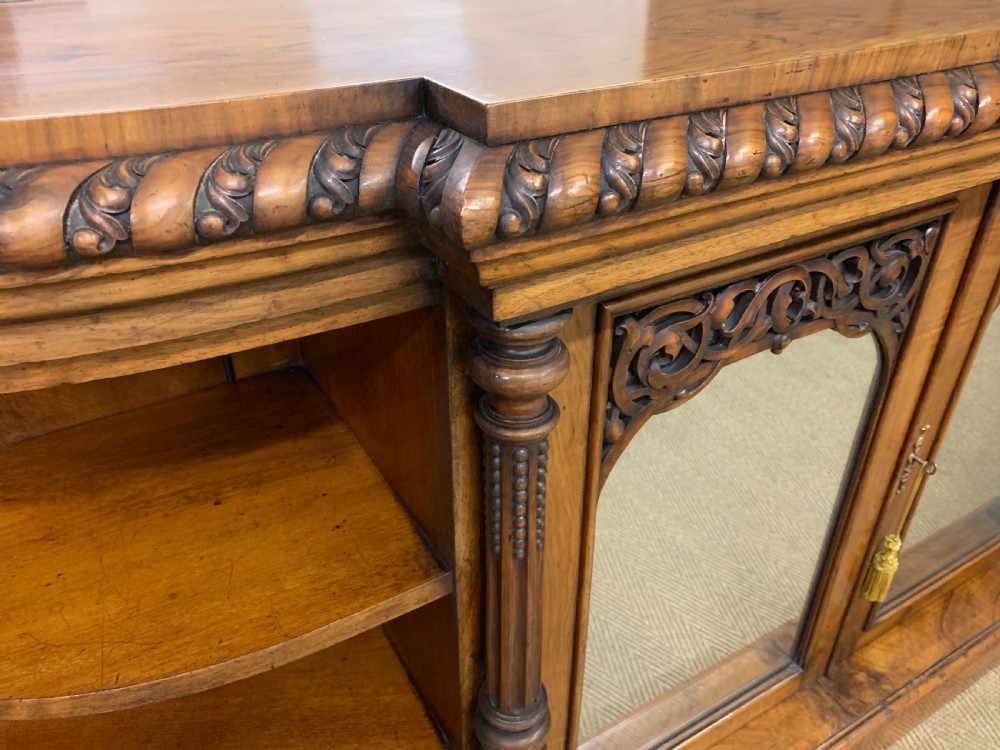 A Victorian burr walnut chiffonier featuring open side display shelves, mirrored central cabinet doors, and an ornate carved mirror frame cresting. View X