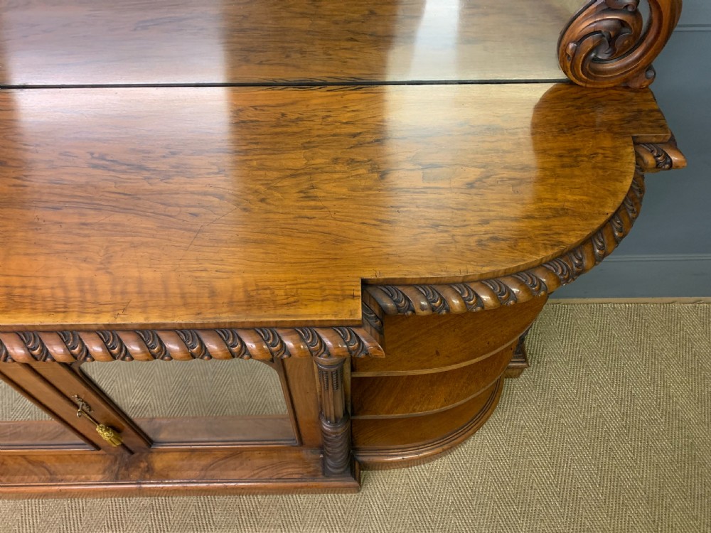 A Victorian burr walnut chiffonier featuring open side display shelves, mirrored central cabinet doors, and an ornate carved mirror frame cresting. View XVI