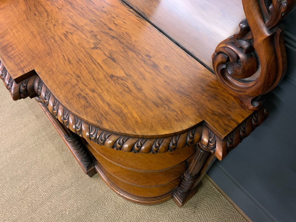 A Victorian burr walnut chiffonier featuring open side display shelves, mirrored central cabinet doors, and an ornate carved mirror frame cresting. View XVIII