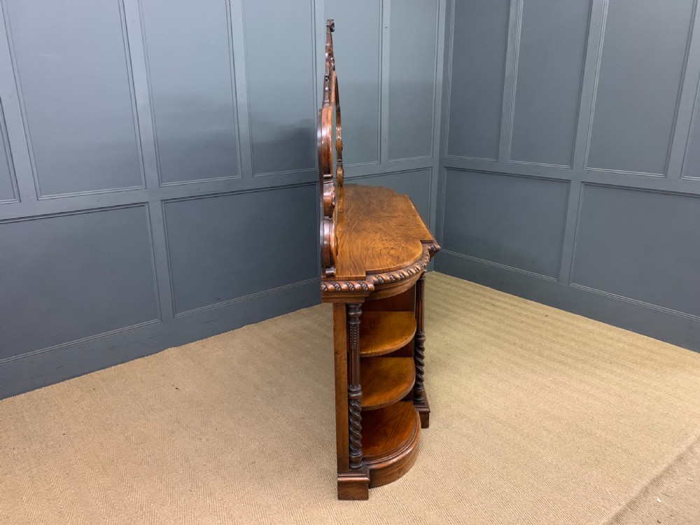 A Victorian burr walnut chiffonier featuring open side display shelves, mirrored central cabinet doors, and an ornate carved mirror frame cresting. View XXIII