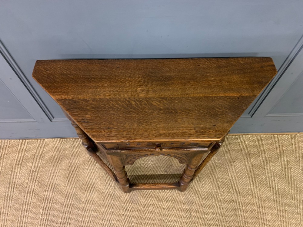 A carved dark oak side table featuring a canted five-sided top, relief carved arches on the frieze, a single drawer, turned legs, and a lower stretcher base. View III