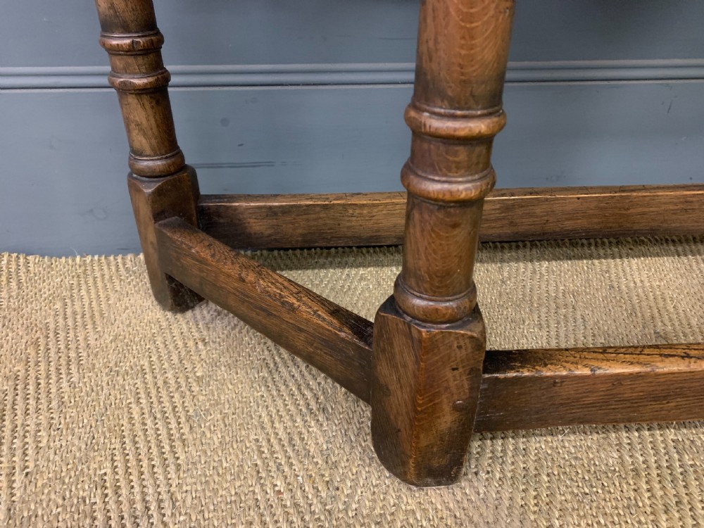 A carved dark oak side table featuring a canted five-sided top, relief carved arches on the frieze, a single drawer, turned legs, and a lower stretcher base. View VI