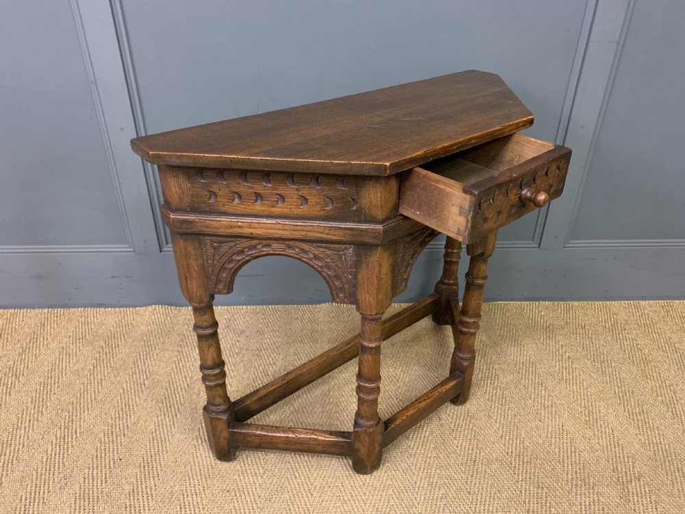 A carved dark oak side table featuring a canted five-sided top, relief carved arches on the frieze, a single drawer, turned legs, and a lower stretcher base. View VIII