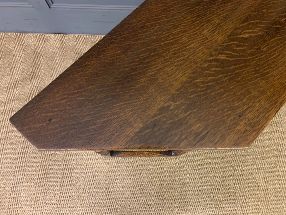 A carved dark oak side table featuring a canted five-sided top, relief carved arches on the frieze, a single drawer, turned legs, and a lower stretcher base. View IX