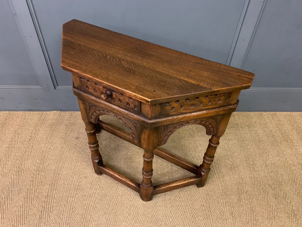 A carved dark oak side table featuring a canted five-sided top, relief carved arches on the frieze, a single drawer, turned legs, and a lower stretcher base. View XI