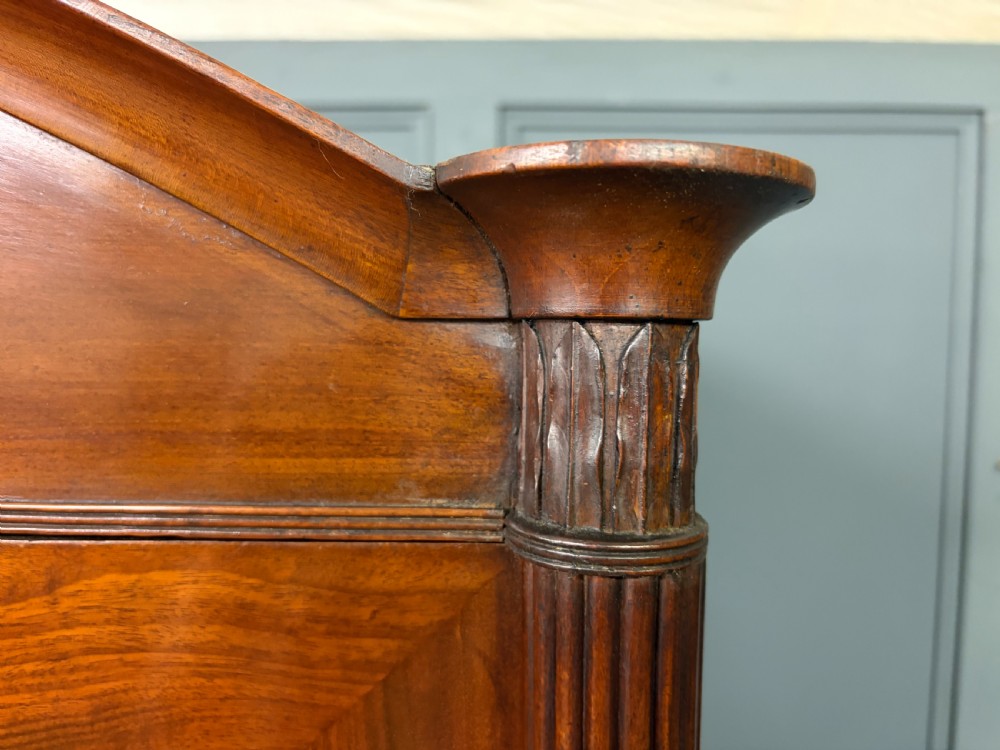 An antique Georgian flame mahogany linen press with an arched top cornice, two inlaid cupboard doors, fluted side pilasters, and a base of five drawers with turned knobs. View V