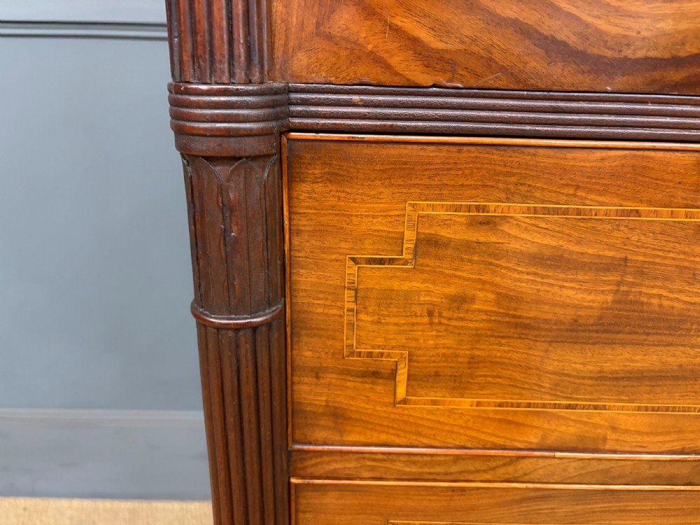 An antique Georgian flame mahogany linen press with an arched top cornice, two inlaid cupboard doors, fluted side pilasters, and a base of five drawers with turned knobs. View VIII