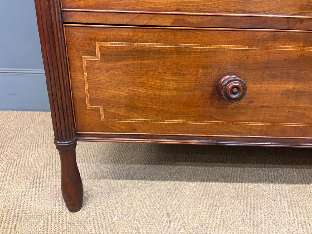 An antique Georgian flame mahogany linen press with an arched top cornice, two inlaid cupboard doors, fluted side pilasters, and a base of five drawers with turned knobs. View IX