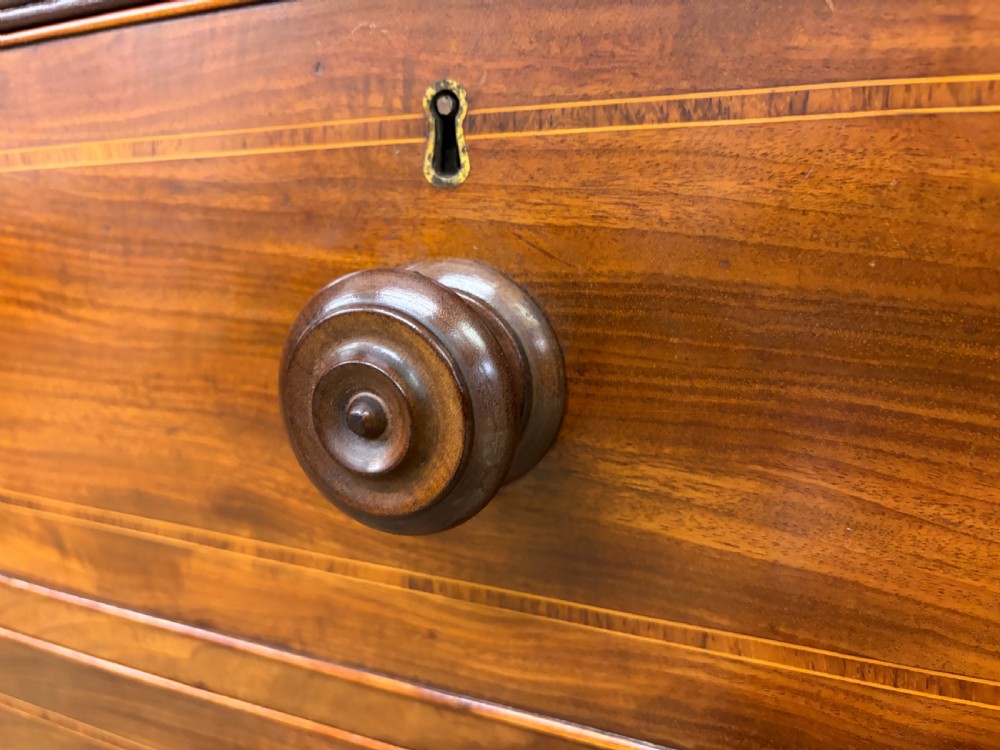An antique Georgian flame mahogany linen press with an arched top cornice, two inlaid cupboard doors, fluted side pilasters, and a base of five drawers with turned knobs. View X