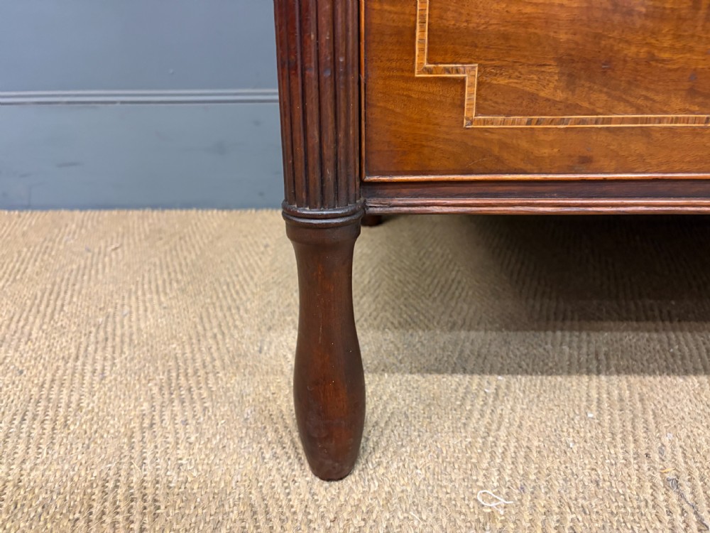 An antique Georgian flame mahogany linen press with an arched top cornice, two inlaid cupboard doors, fluted side pilasters, and a base of five drawers with turned knobs. View XI