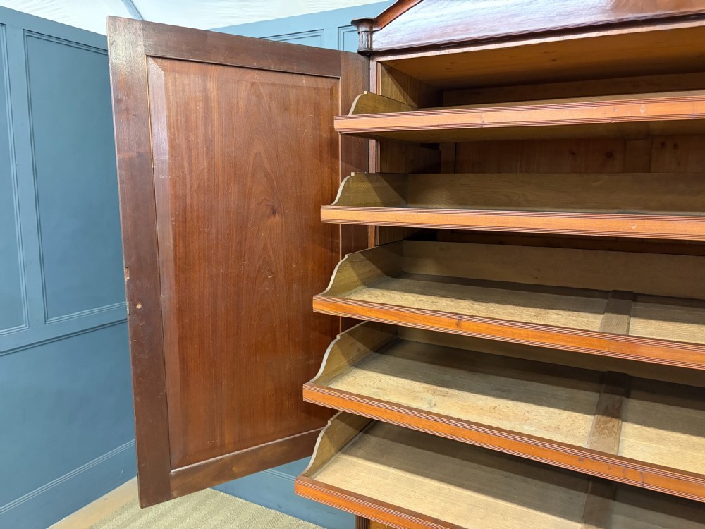 An antique Georgian flame mahogany linen press with an arched top cornice, two inlaid cupboard doors, fluted side pilasters, and a base of five drawers with turned knobs. View XX