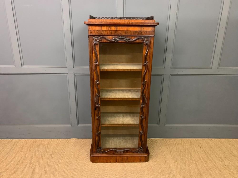 A tall Victorian rosewood bookcase cabinet featuring a single glazed door with carved scrollwork borders and a fretwork top gallery. View II