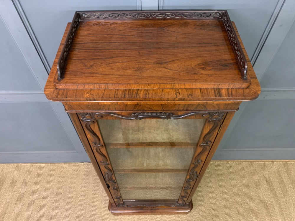 A tall Victorian rosewood bookcase cabinet featuring a single glazed door with carved scrollwork borders and a fretwork top gallery. View IX