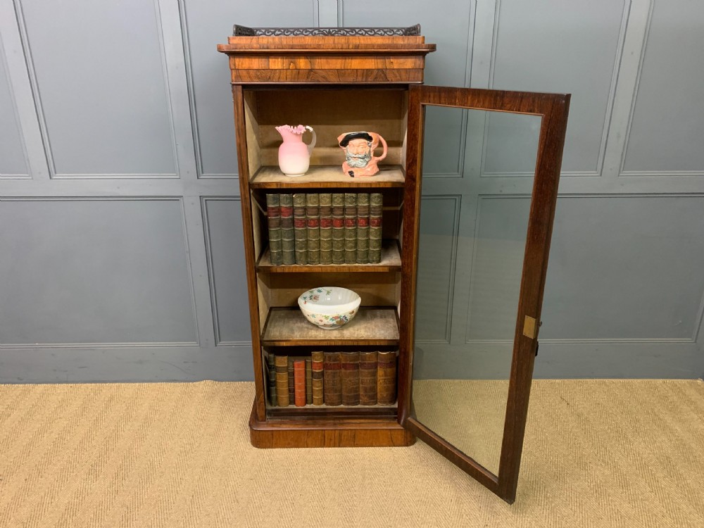 A tall Victorian rosewood bookcase cabinet featuring a single glazed door with carved scrollwork borders and a fretwork top gallery. View XV