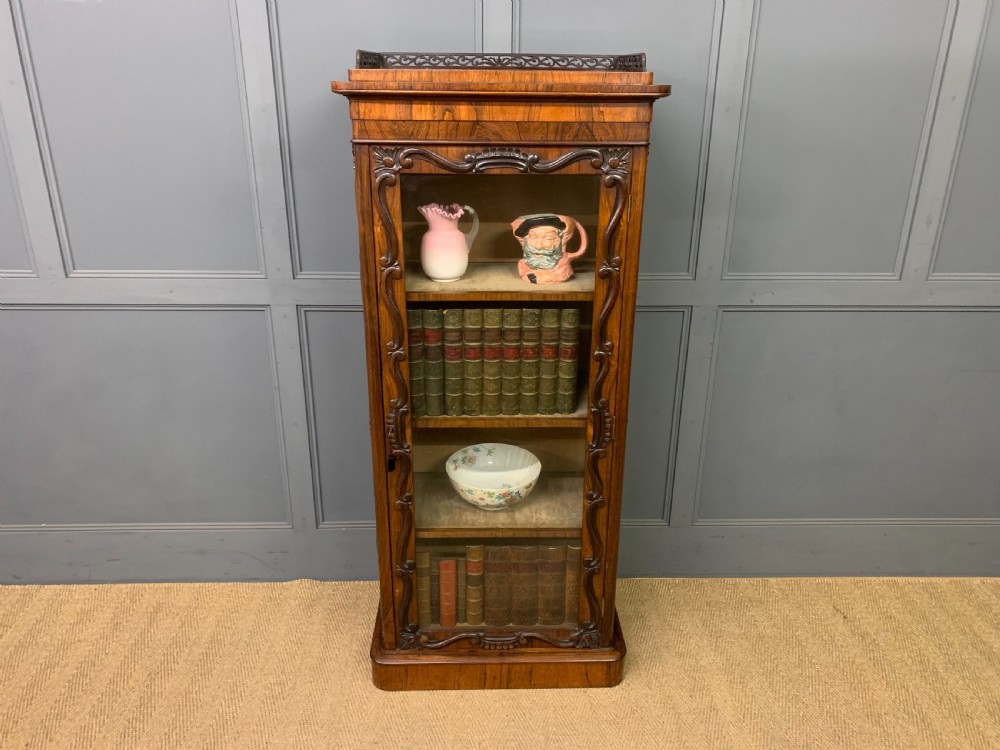 A tall Victorian rosewood bookcase cabinet featuring a single glazed door with carved scrollwork borders and a fretwork top gallery. View XVI