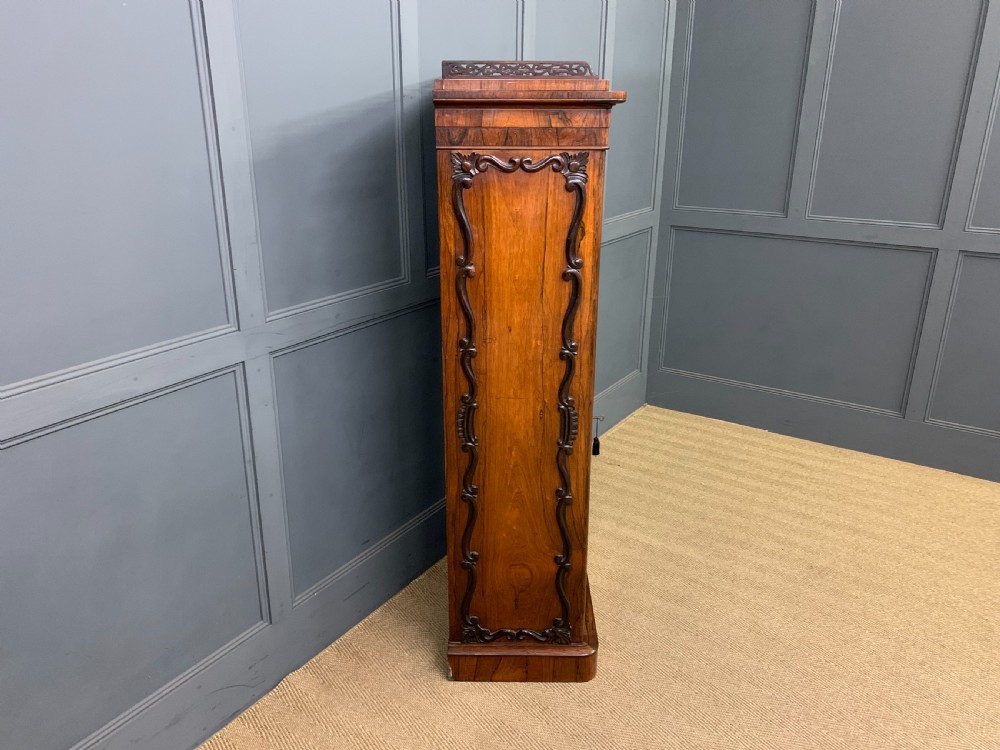 A tall Victorian rosewood bookcase cabinet featuring a single glazed door with carved scrollwork borders and a fretwork top gallery. View XVII
