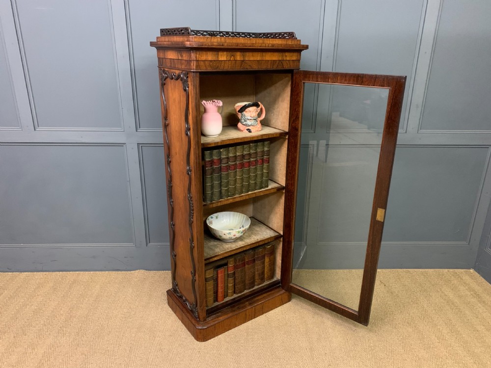 A tall Victorian rosewood bookcase cabinet featuring a single glazed door with carved scrollwork borders and a fretwork top gallery. View XIX